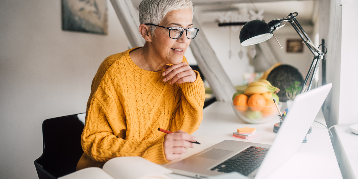 Imagem mulher +50 anos na frente do computador para artigo do blog SoftSell sobre etarismo no setor de tecnologia e as vantagens das empresas de incentivar equipes multigeracionais.